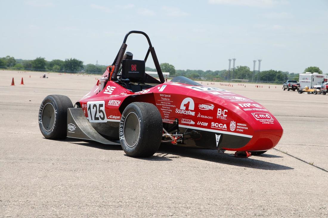 Red race car parked on an open asphalt lot with visible sponsor logos.