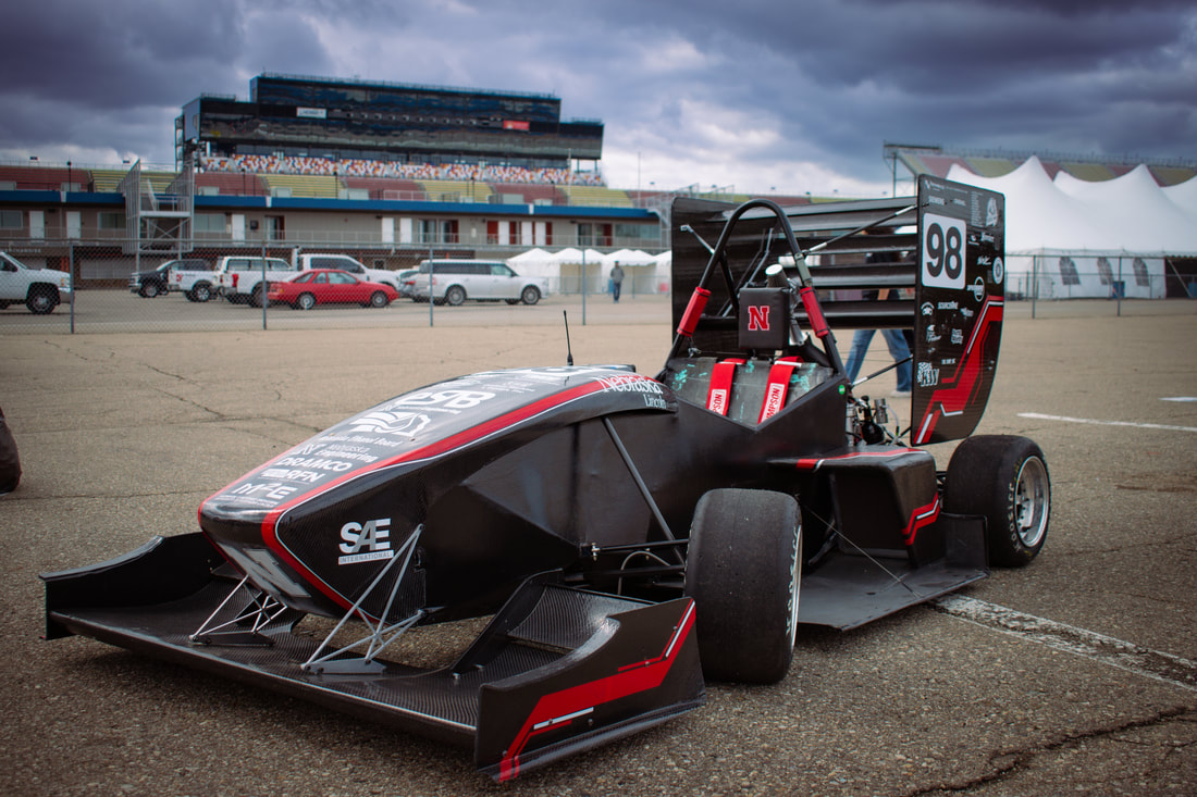 Race car with the number 98 parked on asphalt, with cloudy sky and buildings in the background.
